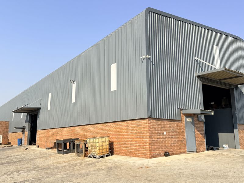 Industrial warehouse facility featuring corrugated metal cladding, face brick base, and multiple roller shutter access points set within a paved yard.