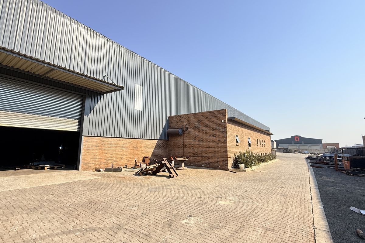 Exterior view of an industrial warehouse featuring a large roller shutter door, brick and metal cladding, and a paved yard area.