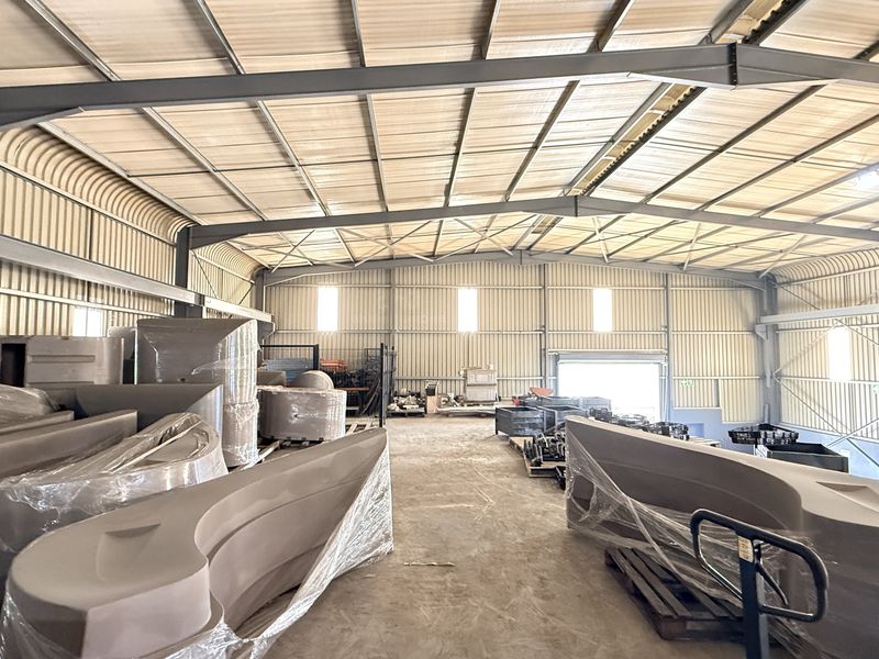 Spacious industrial warehouse featuring a steel portal frame, corrugated metal walls, concrete flooring, and a large roller shutter door for easy access.