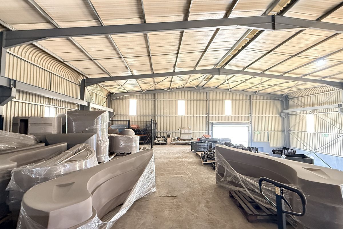 Spacious industrial warehouse featuring a steel portal frame, corrugated metal walls, concrete flooring, and a large roller shutter door for easy access.