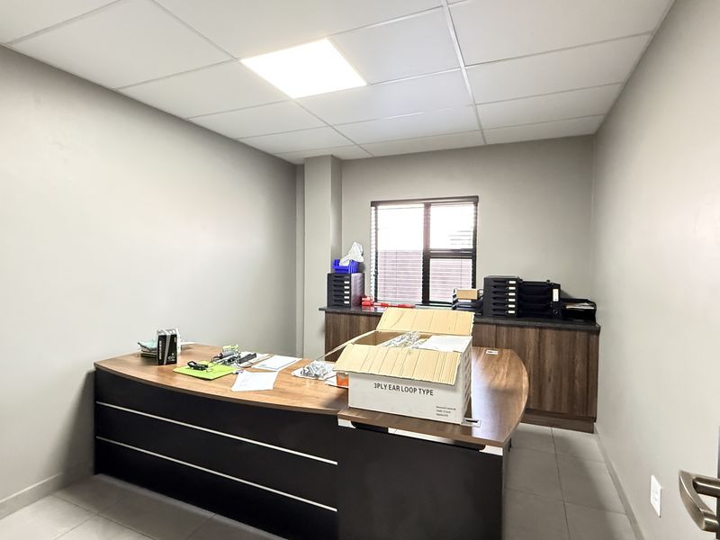 A functional office space featuring neutral walls, tiled flooring, a suspended ceiling with recessed lighting, and built-in cabinetry for storage.