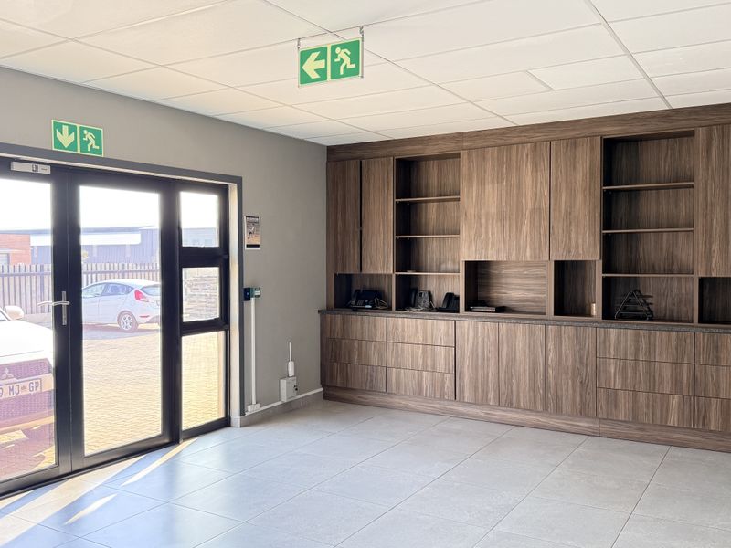 A clean, modern industrial entry area featuring extensive built-in wooden cabinetry, tiled flooring, and a secure double glass door entrance.