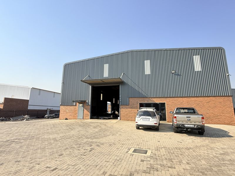 Front view of an industrial warehouse featuring a corrugated metal facade, face brick base, and a large paved yard area.
