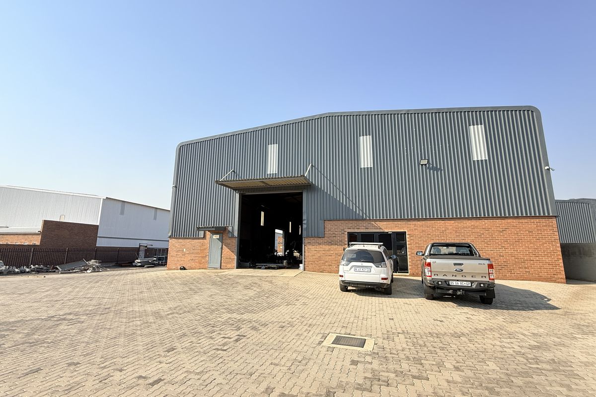 Front view of an industrial warehouse featuring a corrugated metal facade, face brick base, and a large paved yard area.