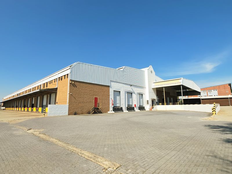 Industrial warehouse facility featuring multiple loading docks, roller shutter doors, a large paved yard, and a covered loading canopy.
