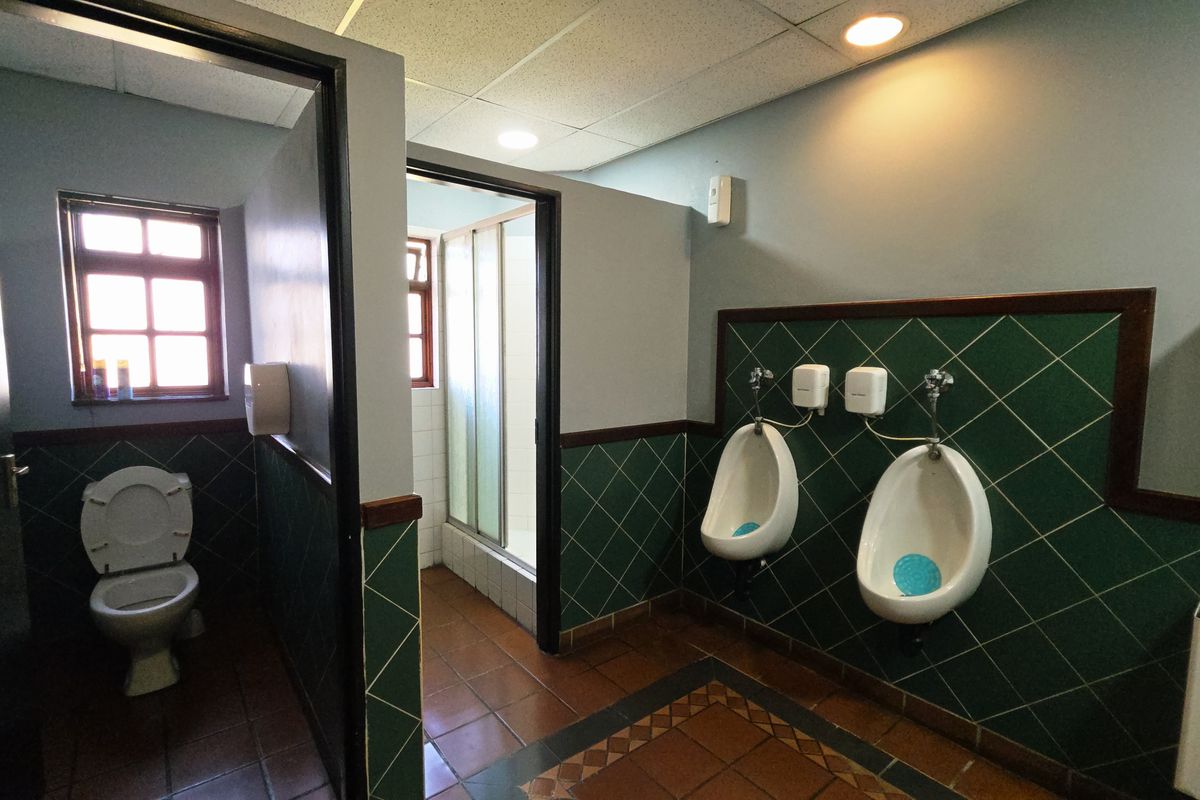 Functional industrial-style bathroom featuring dual urinals, a private toilet cubicle, and a separate shower enclosure with tiled finishes.