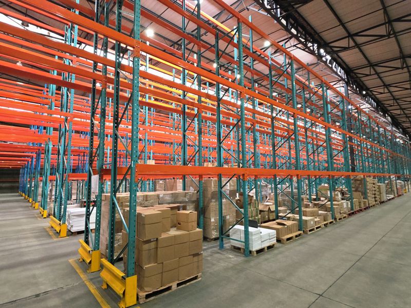 Spacious industrial warehouse facility featuring extensive high-level pallet racking systems, durable concrete flooring, and exposed steel roof structure with high-bay lighting.