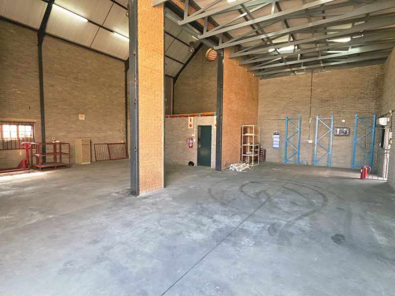 Spacious industrial utility space featuring exposed brick walls, high steel roof trusses, and durable concrete flooring, suitable for storage or workshop operations.