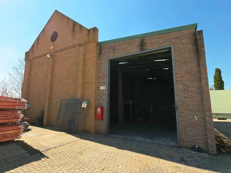 Industrial warehouse exterior featuring a large roller door entrance, brick facade, and paved driveway access.