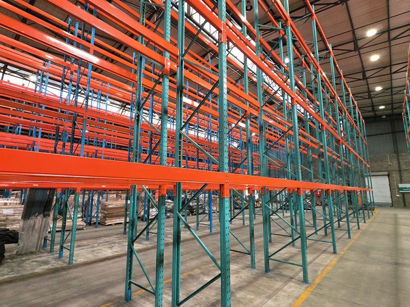 Spacious industrial warehouse interior featuring extensive high-level steel racking systems, polished concrete flooring, and exposed structural roof trusses with high-bay lighting.