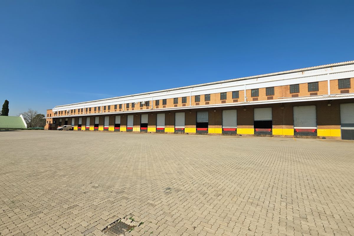 Large industrial warehouse facility featuring multiple loading bays with roller shutter doors and an expansive paved yard area for logistics and transport access.