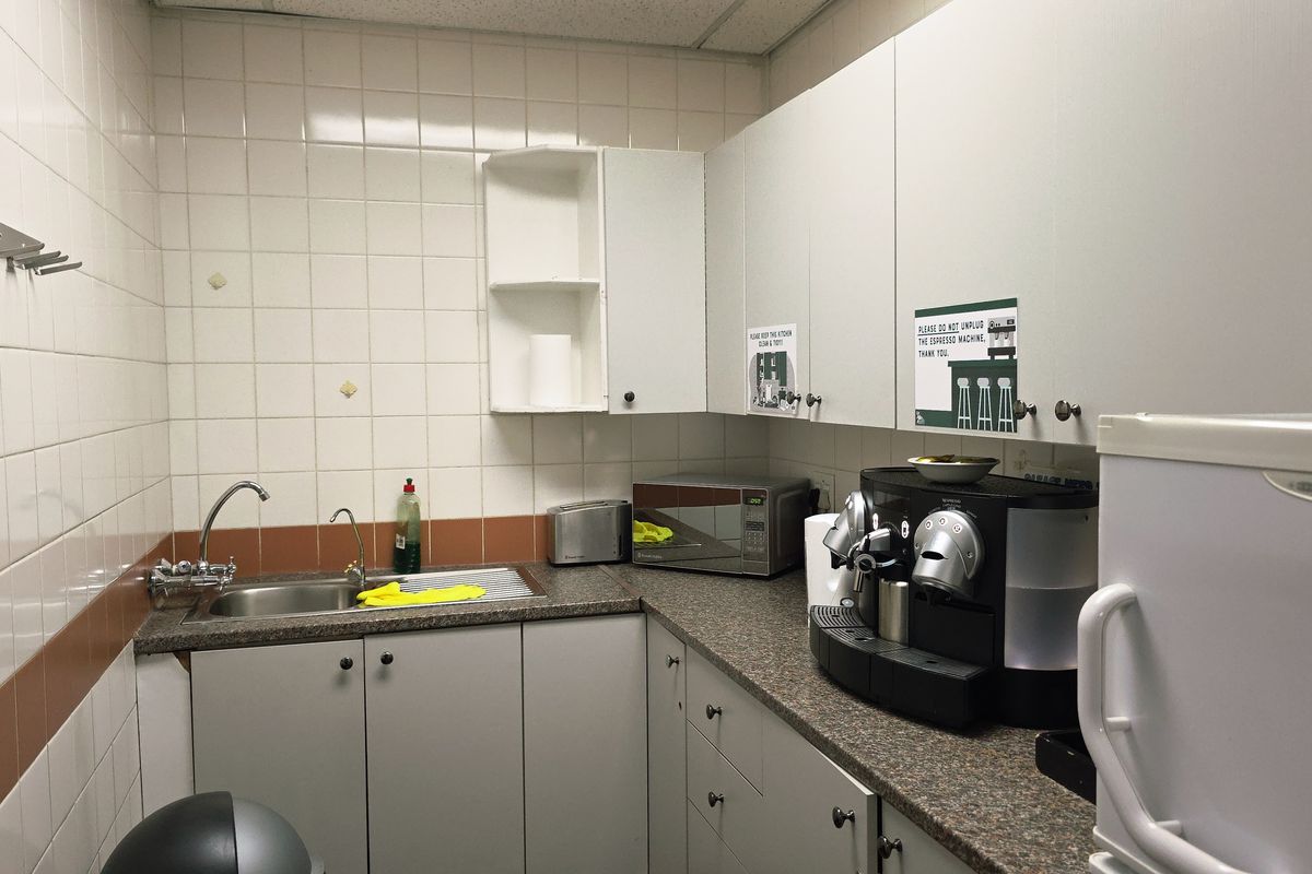 A compact industrial kitchenette featuring laminate countertops, a stainless steel sink, tiled splashback, and functional built-in cabinetry.