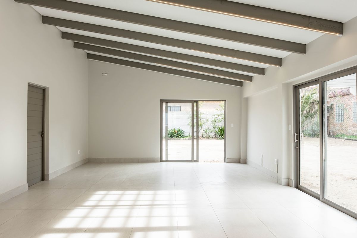 Spacious, light-filled living area featuring exposed ceiling beams, neutral tiled flooring, and large sliding glass doors providing direct access to the rear exterior.