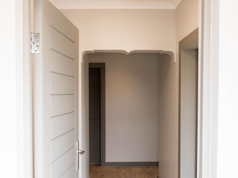 A bright, empty hallway featuring polished timber flooring, neutral wall tones, and modern grey internal doors with matching architraves.