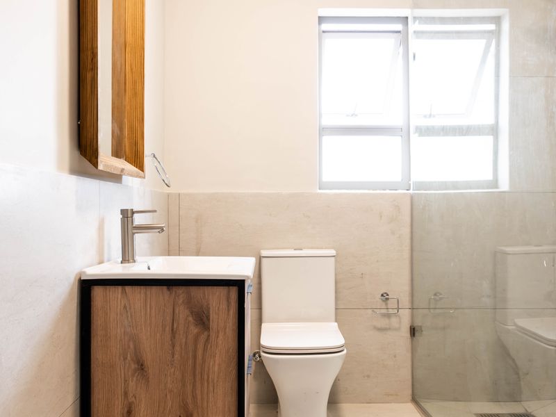 Modern bathroom featuring a wood-finish vanity, walk-in glass shower with rain head, neutral wall tiles, and contemporary fixtures.