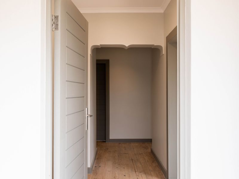 A clean, empty hallway featuring polished timber flooring, neutral wall tones, and a decorative archway leading to adjacent rooms.