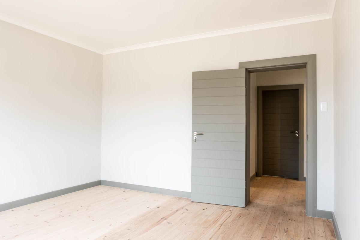 A bright, empty bedroom featuring polished timber flooring, neutral walls, and modern horizontal panelled doors with matching grey frames.