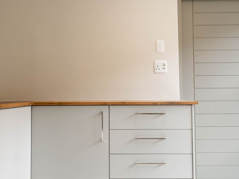 A clean, modern kitchen area featuring light grey cabinetry, a natural wood countertop, and a matching internal door.