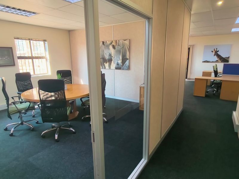 A professional office space featuring a glass-partitioned meeting room, suspended ceilings, recessed lighting, and carpeted flooring throughout.