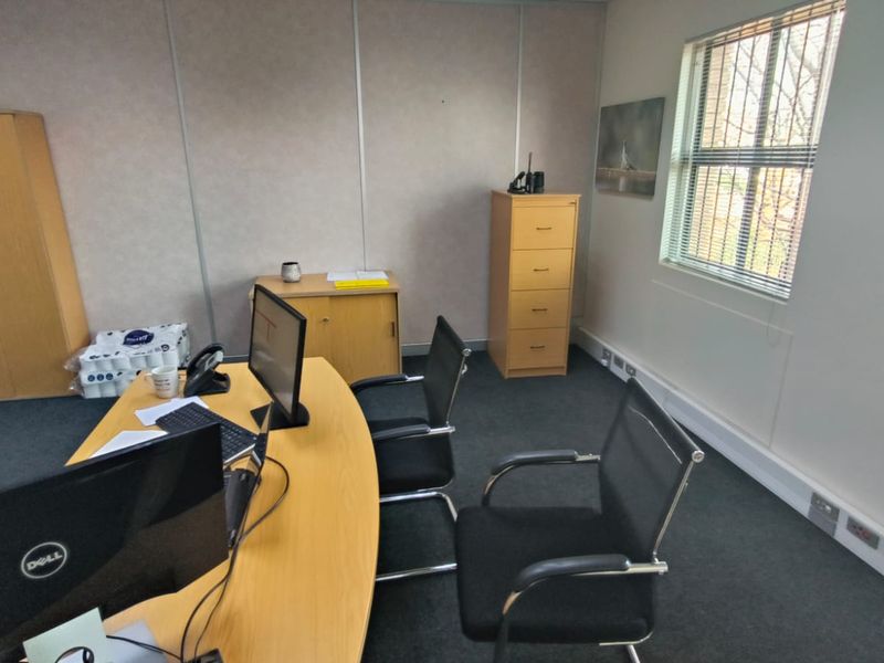 A functional office space featuring modular wall panels, carpeted flooring, and a window with security bars, providing a practical work environment.