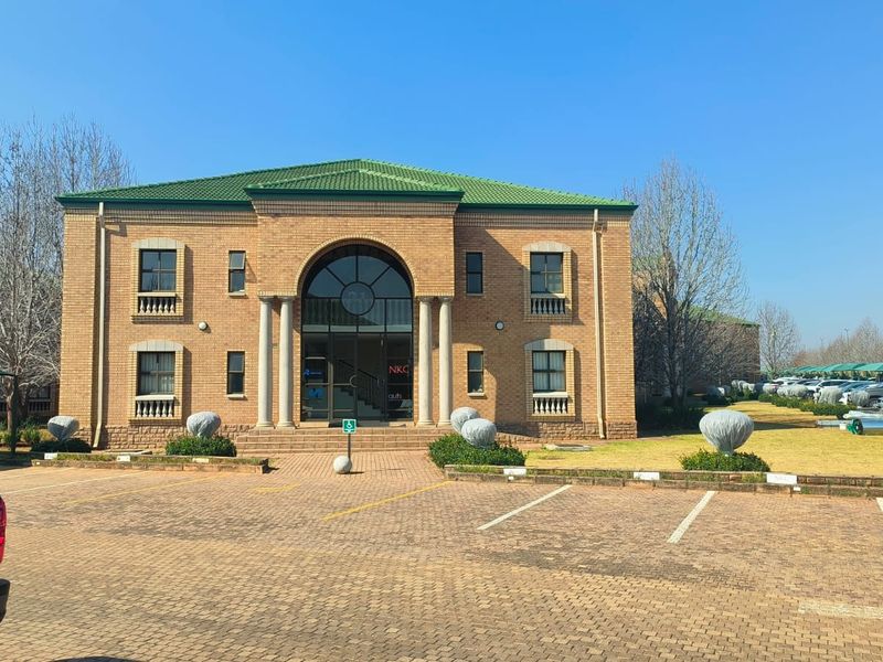 Front elevation of a two-story brick office building featuring an arched entrance, columns, and a paved parking area.