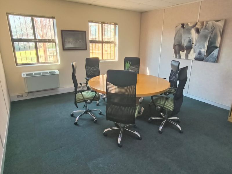 A functional office meeting room featuring modular wall panels, carpeted flooring, and a wall-mounted air conditioning unit with security bars on the windows.