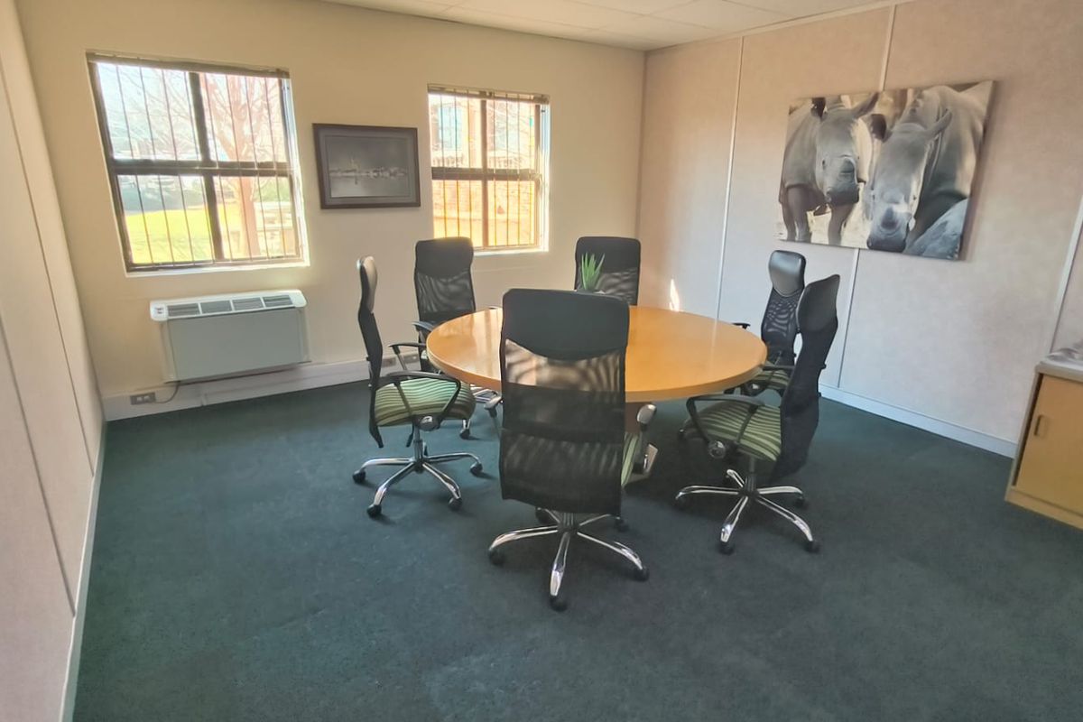 A functional office meeting room featuring modular wall panels, carpeted flooring, and a wall-mounted air conditioning unit with security bars on the windows.