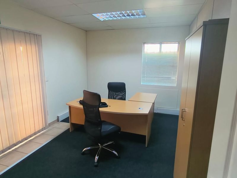 A functional office space featuring carpeted flooring, suspended ceiling with recessed lighting, and window blinds for privacy and light control.