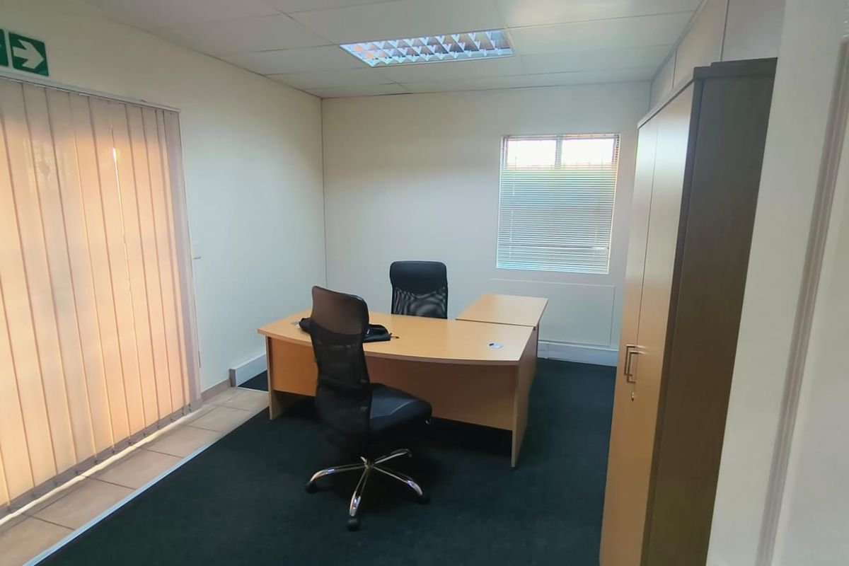A functional office space featuring carpeted flooring, suspended ceiling with recessed lighting, and window blinds for privacy and light control.