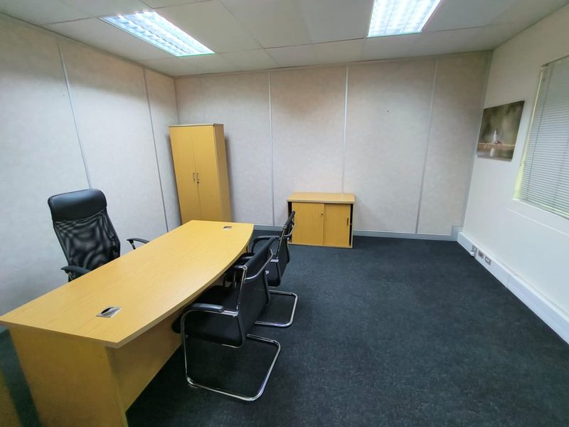 A functional office space featuring modular wall panels, suspended ceiling with recessed lighting, and dark carpet flooring, suitable for a professional work environment.