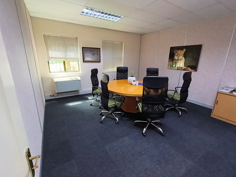 A functional office space featuring carpeted flooring, a suspended ceiling with recessed lighting, and a wall-mounted air conditioning unit.
