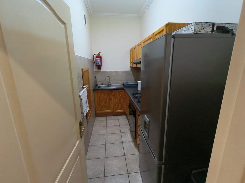 A compact office kitchen featuring wooden cabinetry, tiled flooring, a stainless steel sink, and built-in cooking appliances.