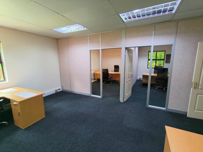 A functional office space featuring partitioned rooms, suspended ceilings with recessed lighting, and carpeted flooring, providing a professional environment for business operations.
