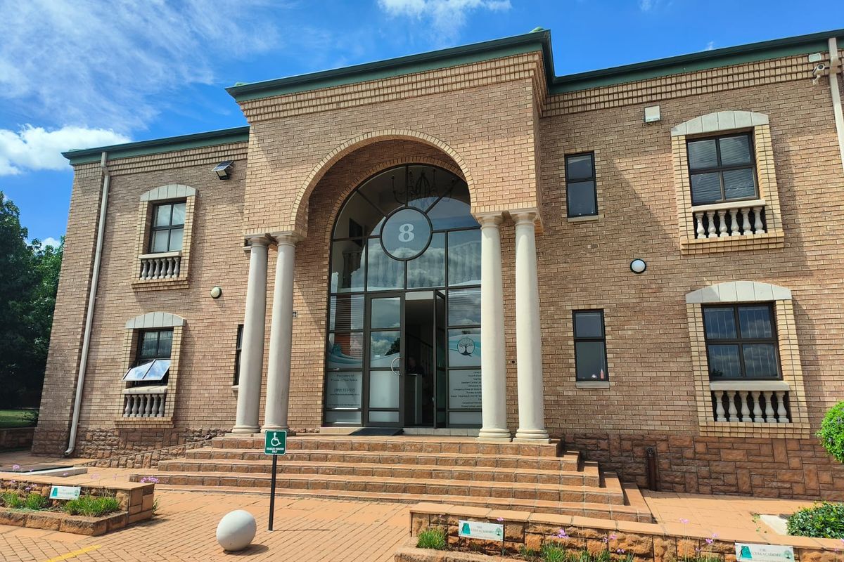 A professional front elevation of a brick office building featuring an arched entrance, decorative columns, and paved access with handicap parking.