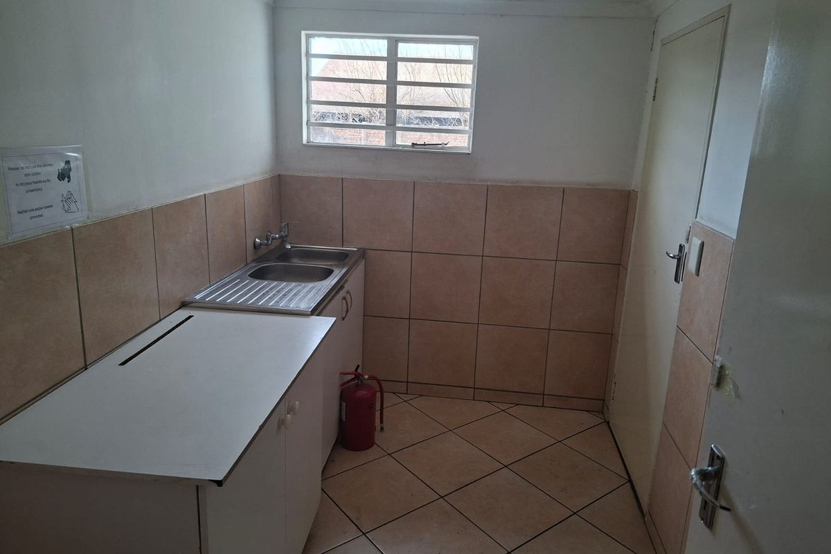 A functional kitchenette area featuring tiled walls and flooring, a stainless steel sink, and a window with security bars.