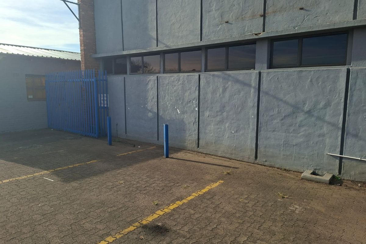 Rear exterior view of the office building featuring a paved parking area, security fencing, and a painted concrete facade with horizontal windows.
