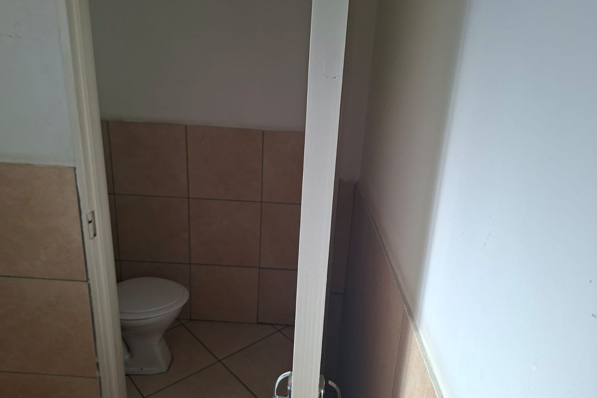 A small, functional office restroom featuring ceramic wall and floor tiling with a standard toilet fixture.