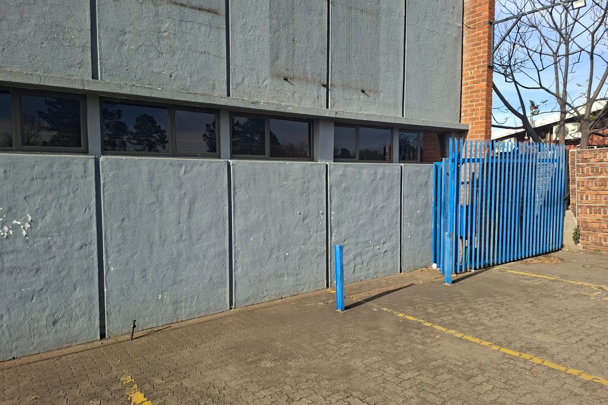 Rear exterior view of the office building featuring a paved parking area, security fencing, and a painted concrete facade with strip windows.