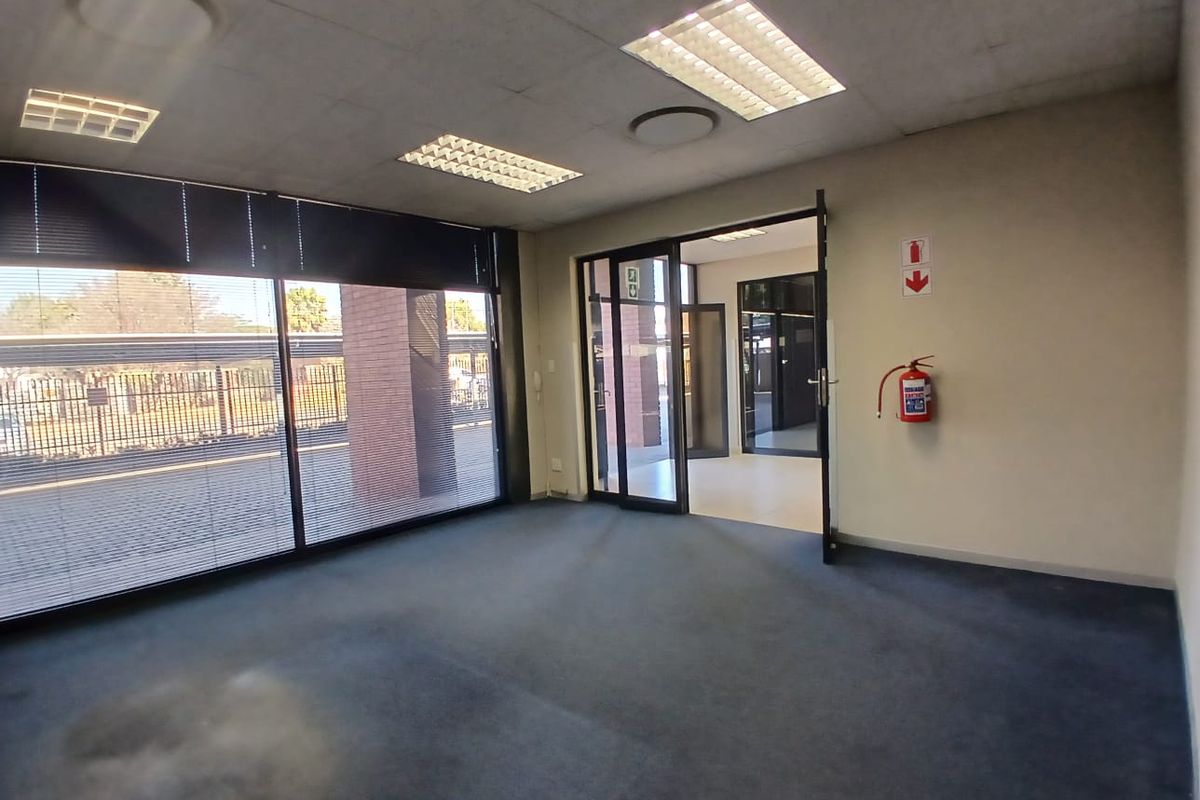 An empty office space featuring large windows, suspended ceilings with recessed lighting, and carpeted flooring, providing a functional and professional work environment.
