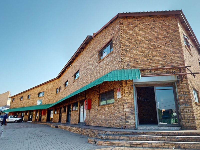 A commercial building featuring a face brick facade, green metal awning, and paved entrance area with multiple glass access points.