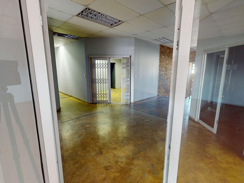 An empty commercial office space featuring exposed brickwork, concrete flooring, suspended ceilings, and secure internal partitioning.