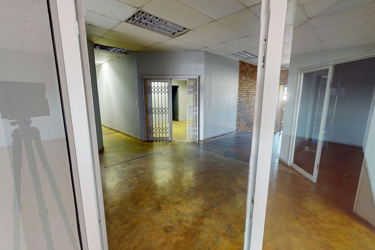 An empty commercial office space featuring exposed brickwork, concrete flooring, suspended ceilings, and secure internal partitioning.