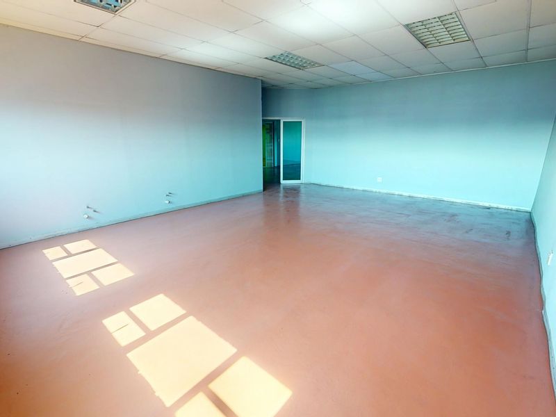 An empty commercial office space featuring a suspended ceiling, recessed lighting, painted concrete flooring, and an exposed brick feature wall.