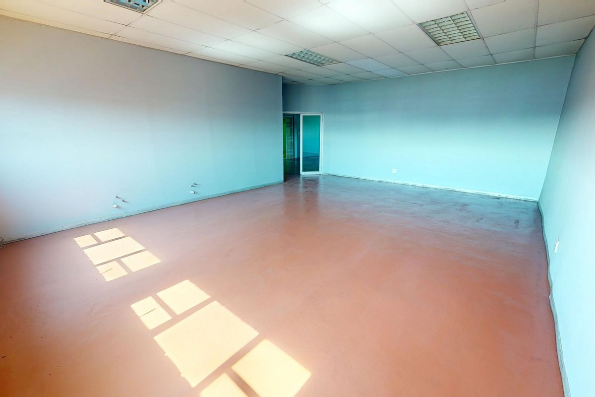An empty commercial office space featuring a suspended ceiling, recessed lighting, painted concrete flooring, and an exposed brick feature wall.