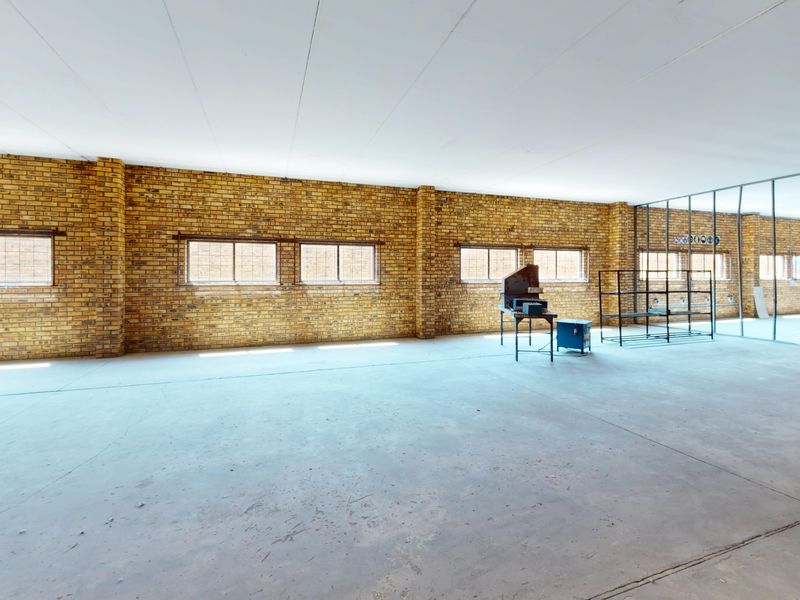 Spacious open-plan commercial area featuring exposed brick walls, concrete flooring, and large windows, offering a versatile blank canvas for various business configurations.
