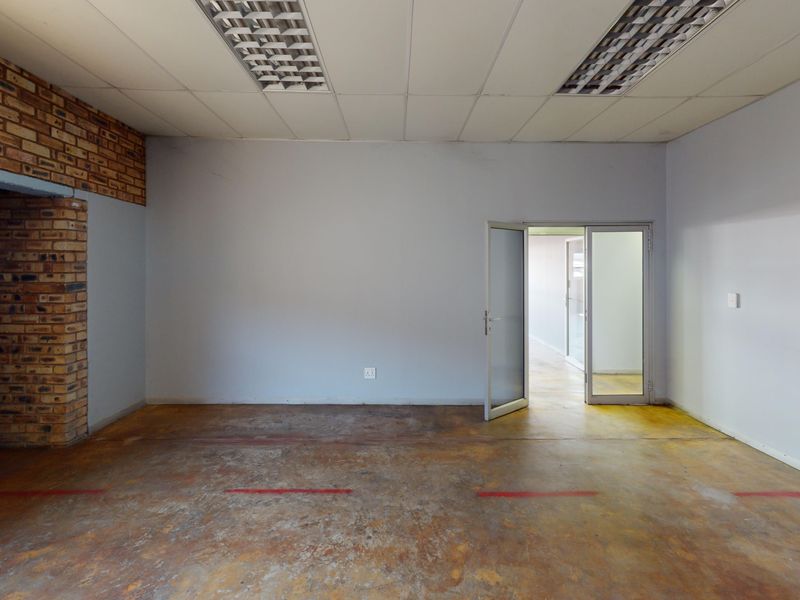 An empty commercial office space featuring exposed brick accents, a suspended ceiling with integrated lighting, and durable concrete flooring.