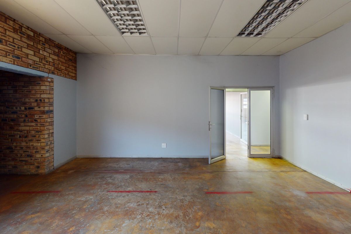 An empty commercial office space featuring exposed brick accents, a suspended ceiling with integrated lighting, and durable concrete flooring.