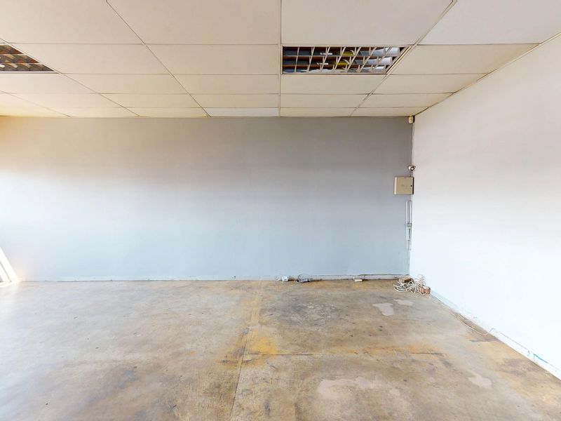An empty commercial office space featuring a suspended ceiling, exposed brick accents, and concrete flooring, suitable for a variety of business configurations.