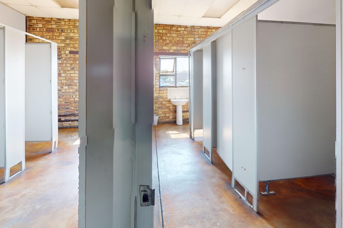 Commercial bathroom facility featuring partitioned cubicles, exposed brick walls, and a pedestal basin, currently in need of refurbishment.
