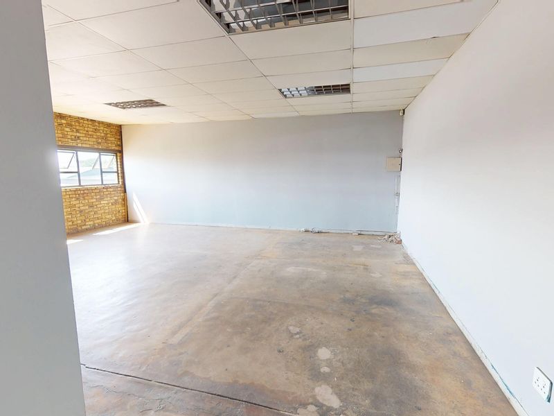 An empty, open-plan commercial office space featuring exposed brickwork, concrete flooring, and a suspended ceiling with recessed lighting.